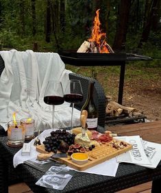 a table with wine, cheese and meats on it next to a fire pit