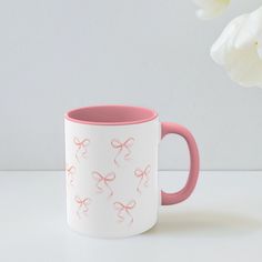 a pink and white coffee mug with bows on the inside sits next to a flower