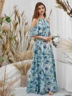 a woman in a blue and white floral print dress standing next to tall grass plants