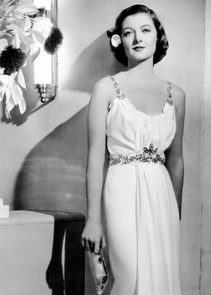 a woman in a long white dress standing next to a mirror with flowers on it