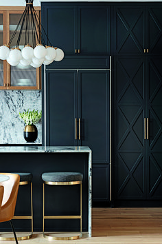 an image of a kitchen with black cabinets and marble counter tops, gold accents on the bar stools