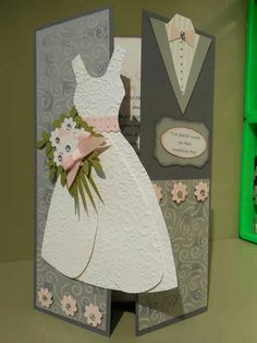 a card with a wedding dress on it and flowers in the front, sitting next to a green box