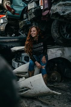 a woman sitting on top of a pile of junk in front of a wrecked car