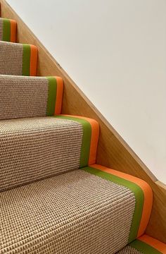 an orange and green striped carpeted stair case next to a white wall with a wooden handrail