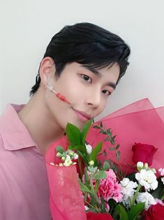 a young man holding a bouquet of flowers in front of his face and looking at the camera