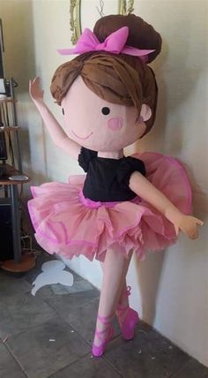 a stuffed ballerina doll in a pink tutu and black top, standing against a wall