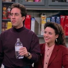 a man and woman standing next to each other in front of a shelf with bottles