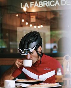 a man sitting at a table with a coffee cup in his hand and wearing a helmet