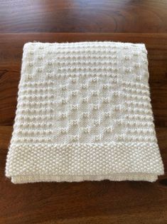 a white knitted blanket sitting on top of a wooden floor