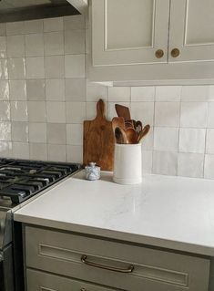 a kitchen counter with utensils in a white ceramic container next to an oven