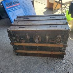 an old trunk sitting on the ground next to a bed rail sign and other items