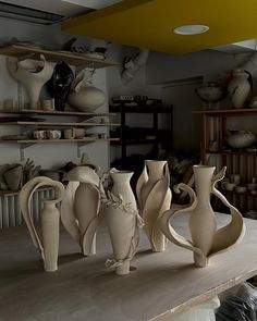 several white vases sitting on top of a wooden table in a room filled with shelves