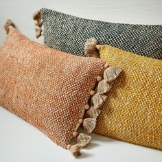 three different colored pillows with tassels on them