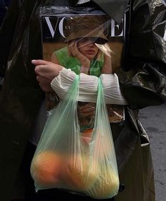 a woman holding a plastic bag full of oranges and an apple in her hand