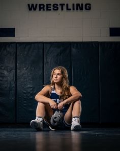 a woman sitting on the floor with her feet up in front of her and holding a wrestling glove