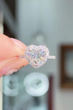 a heart shaped diamond ring being held by someone's hand