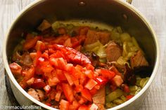 a pot filled with meat and vegetables on top of a wooden table next to utensils