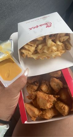 a person holding two boxes with food in them and dipping sauce on the other side