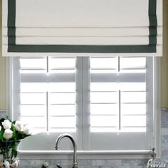 a kitchen sink under a window with white roses in the vase on the counter top