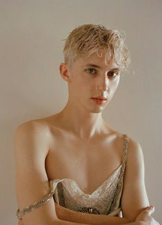 a woman with blonde hair wearing a white dress and posing for the camera in front of a wall