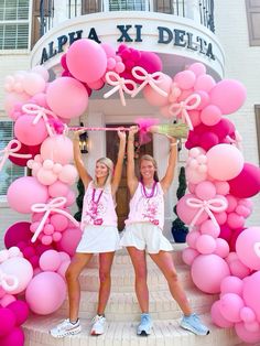 two girls are holding up pink balloons in front of a building that says aria xi delta