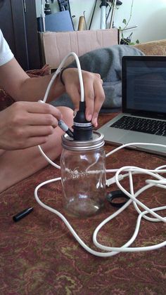 a person is plugging wires into a mason jar with a laptop in the background