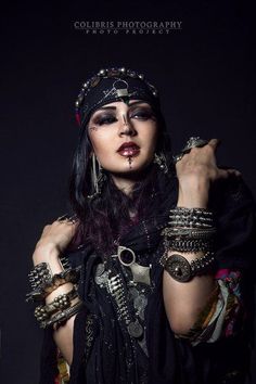 a woman with black hair and jewelry on her face posing for a photo in front of a dark background