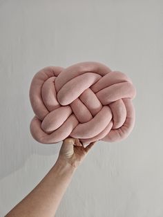 a hand holding up a large pink knot pillow