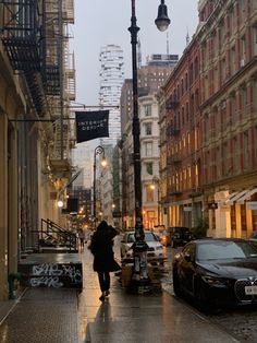 a person walking down a street in the rain with an umbrella over their head and cars parked on the side walk