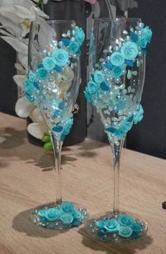 two wine glasses decorated with blue flowers and pearls on a table next to a vase