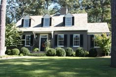 a gray house with black shutters and white trim on the front door is surrounded by green grass