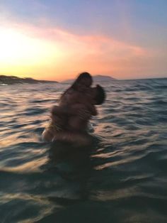 two people are hugging in the ocean at sunset or sunrise, while one person is on his back