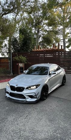 a silver sports car parked in front of a wooden fence and tree lined driveway area