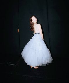 a woman in a white dress is standing on a black floor with her back to the camera