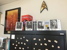 books and pictures are on top of a bookcase in front of a star trek poster