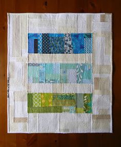 a quilted wall hanging on the side of a wooden wall with multiple strips of blue, green and white fabric