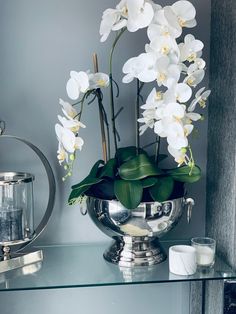 white flowers in a silver vase on a glass table next to a mirror and teapot