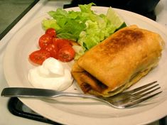 a white plate topped with food next to a fork and salad on top of a table