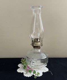 an old fashioned glass oil lamp on a doily with flowers in the bottom half