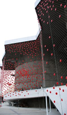 red balls are floating in the air near a building with a large screen on it's side