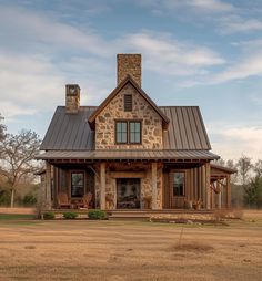 a stone house with a metal roof and porches on an open field in front of trees