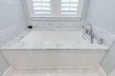 a white bathroom with marble counter tops and tile flooring, along with two windows