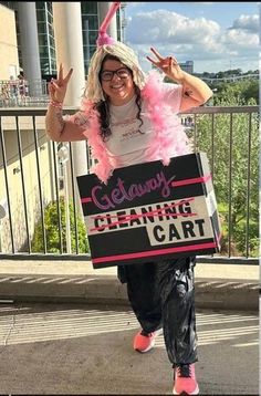 a woman is walking down the street with a cleaning cart sign on her head and pink feathers