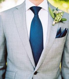 a man in a gray suit with a blue tie and flower boutonniere