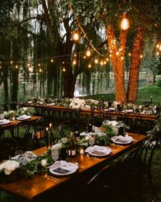 an outdoor dinner table set up with white flowers and greenery, hanging lights over the tables