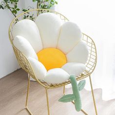 a white and yellow flower shaped chair sitting on top of a wooden floor next to a potted plant