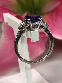 a blue diamond ring sitting on top of a white stand with pink flowers in the background