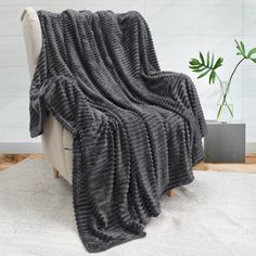 a gray blanket sitting on top of a white chair next to a potted plant