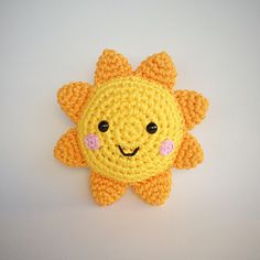 a crocheted yellow sunflower with pink eyes on it's face, sitting in front of a white background