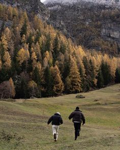 two people are running in the grass near mountains